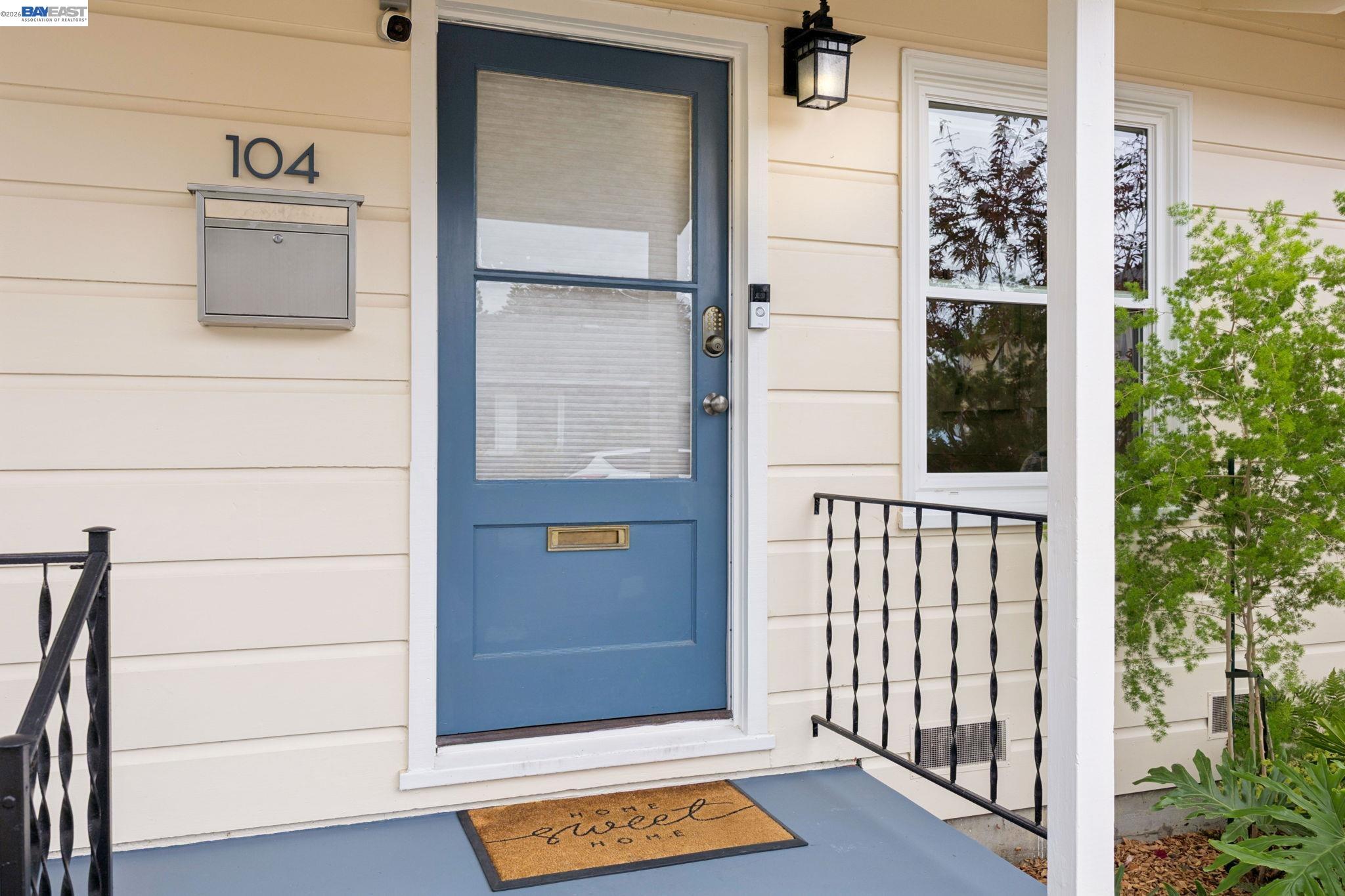 Front entrance with a blue door, cream siding, black railings, and a mailbox marked 104.