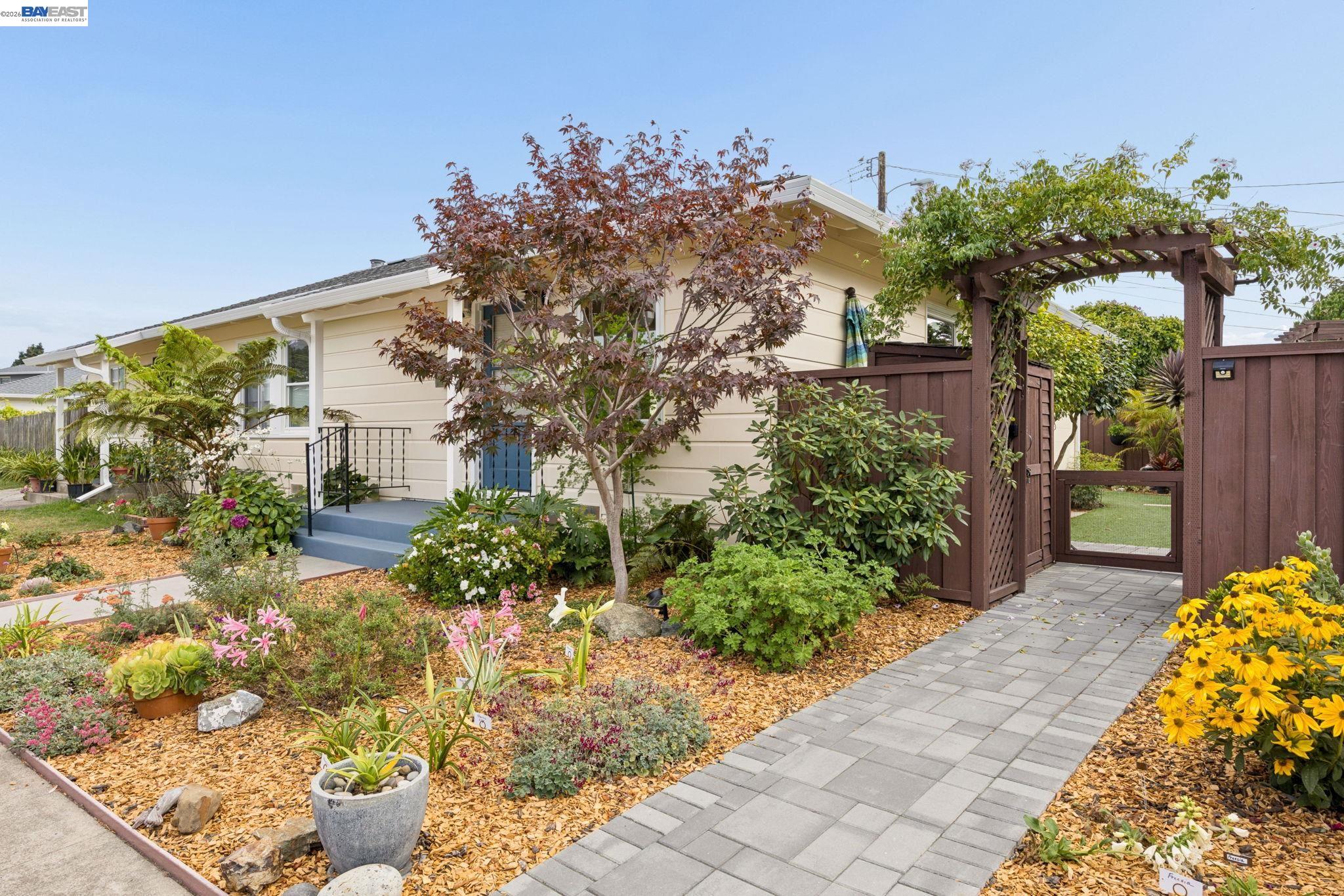 Home exterior with a landscaped flower garden, blue porch, and vine-covered pergola gate.