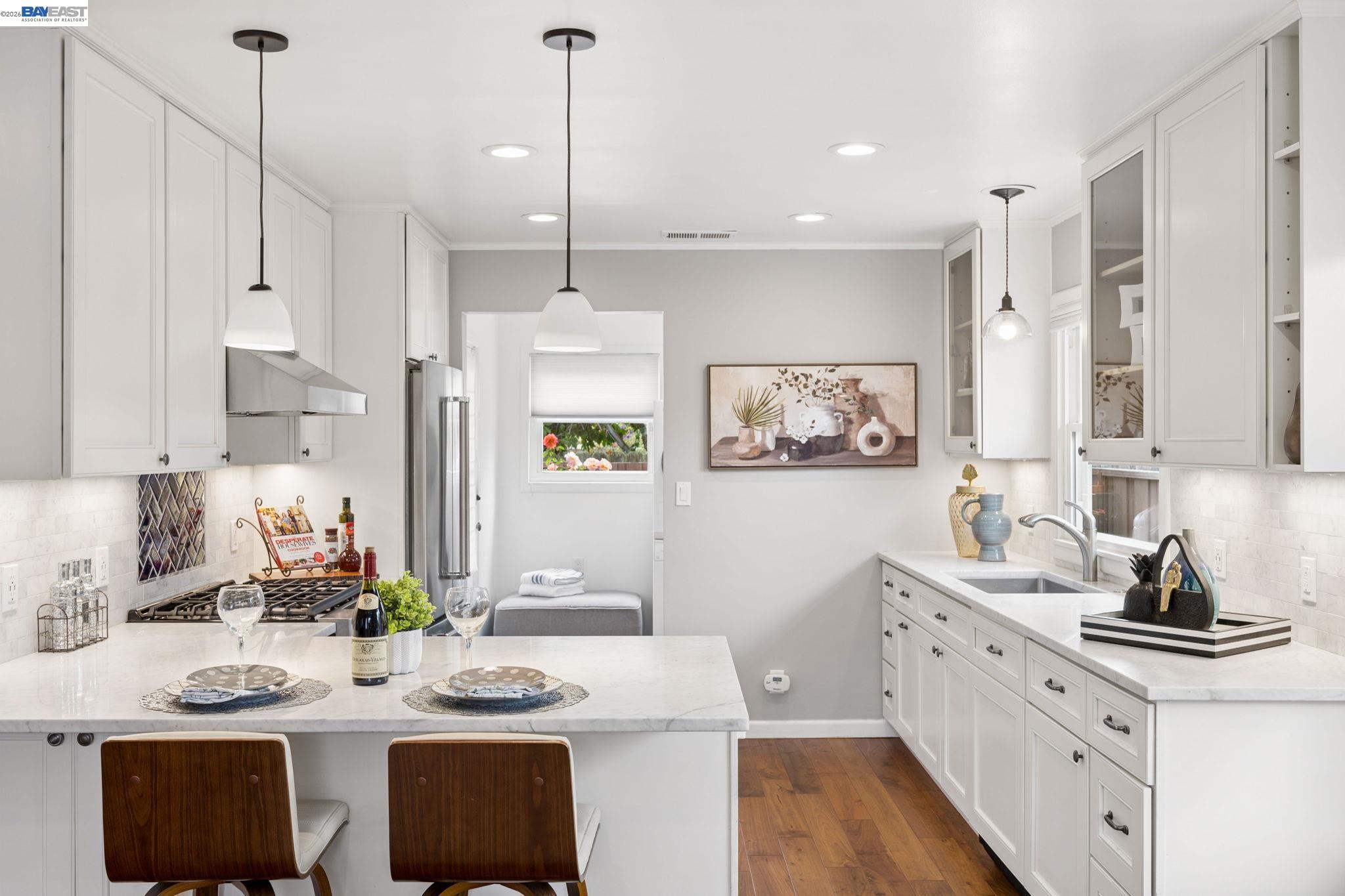 Bright white kitchen with a set dining island, stainless steel appliances, and warm wood floors.
