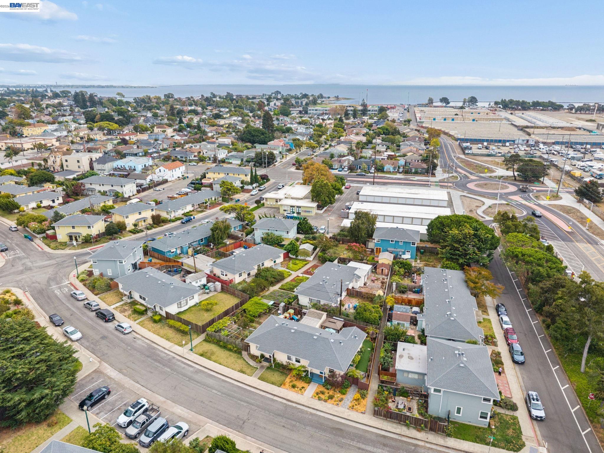 Aerial view of a residential neighborhood beside the bay, with a roundabout and nearby industrial complex.