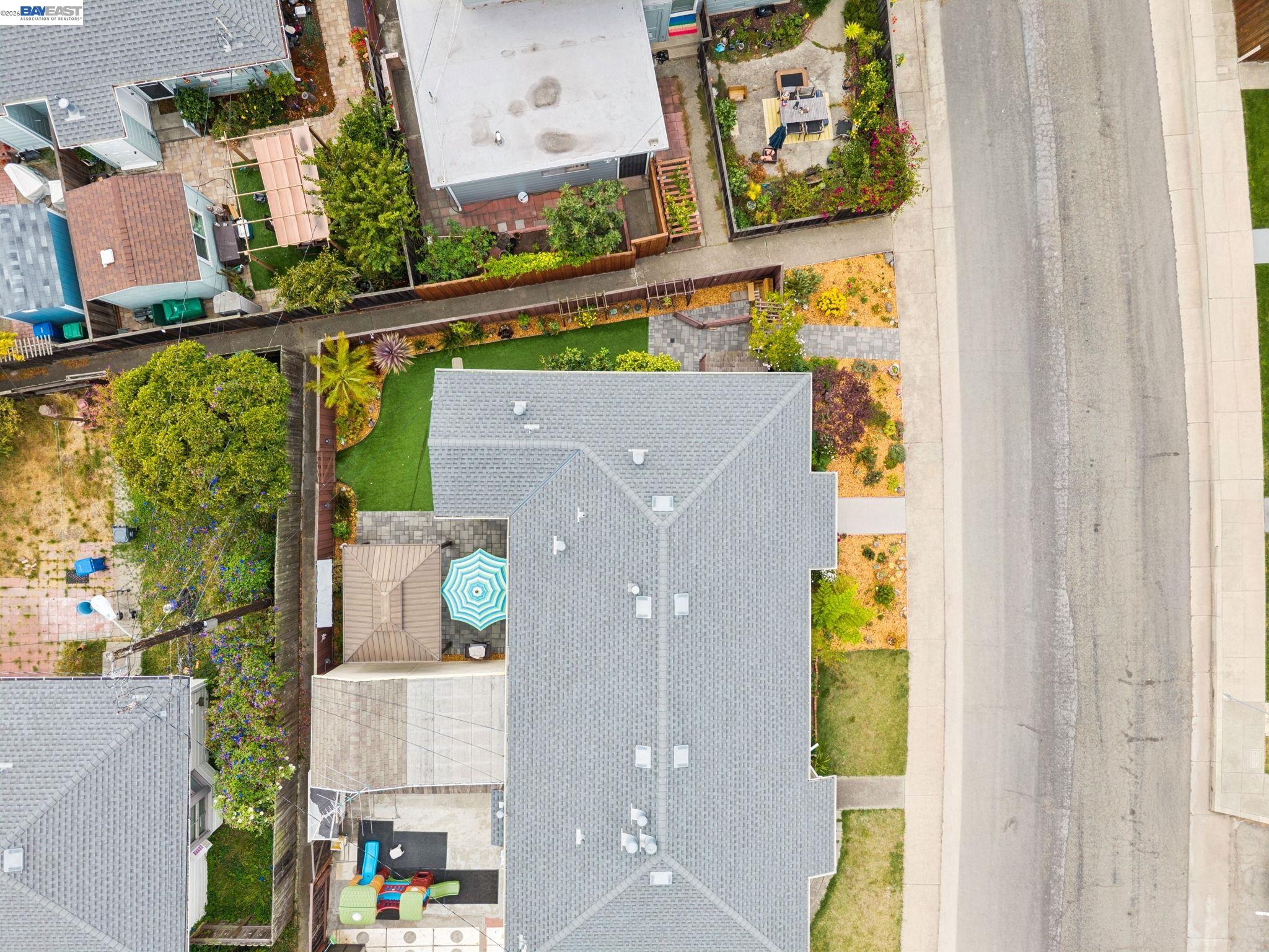 Aerial view of 104 Cypress St, with landscaped yards, patio areas, and a striped umbrella beside the gray roof.