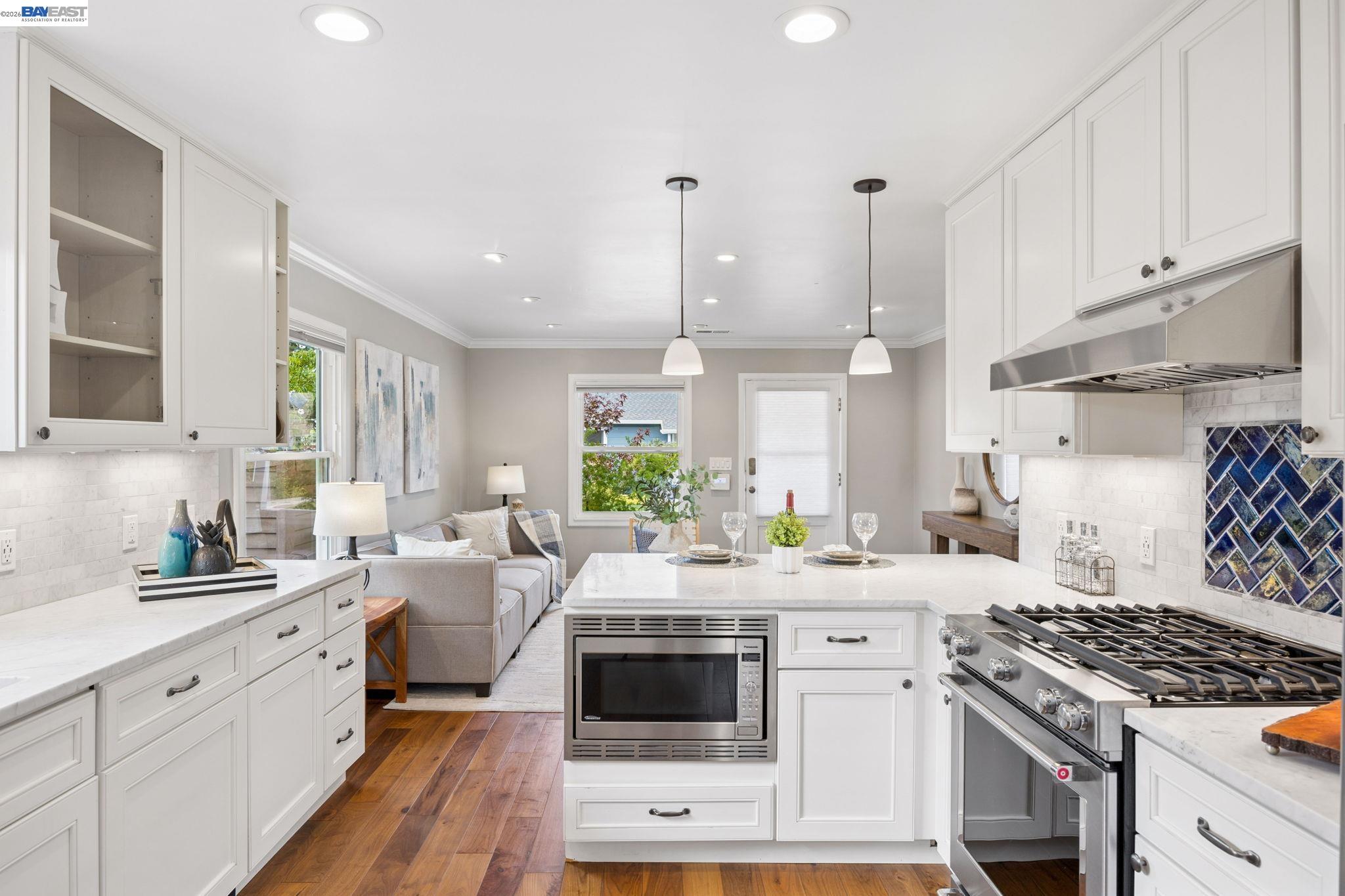 Bright white kitchen with a large stainless range, blue tile backsplash, and island with built-in microwave.