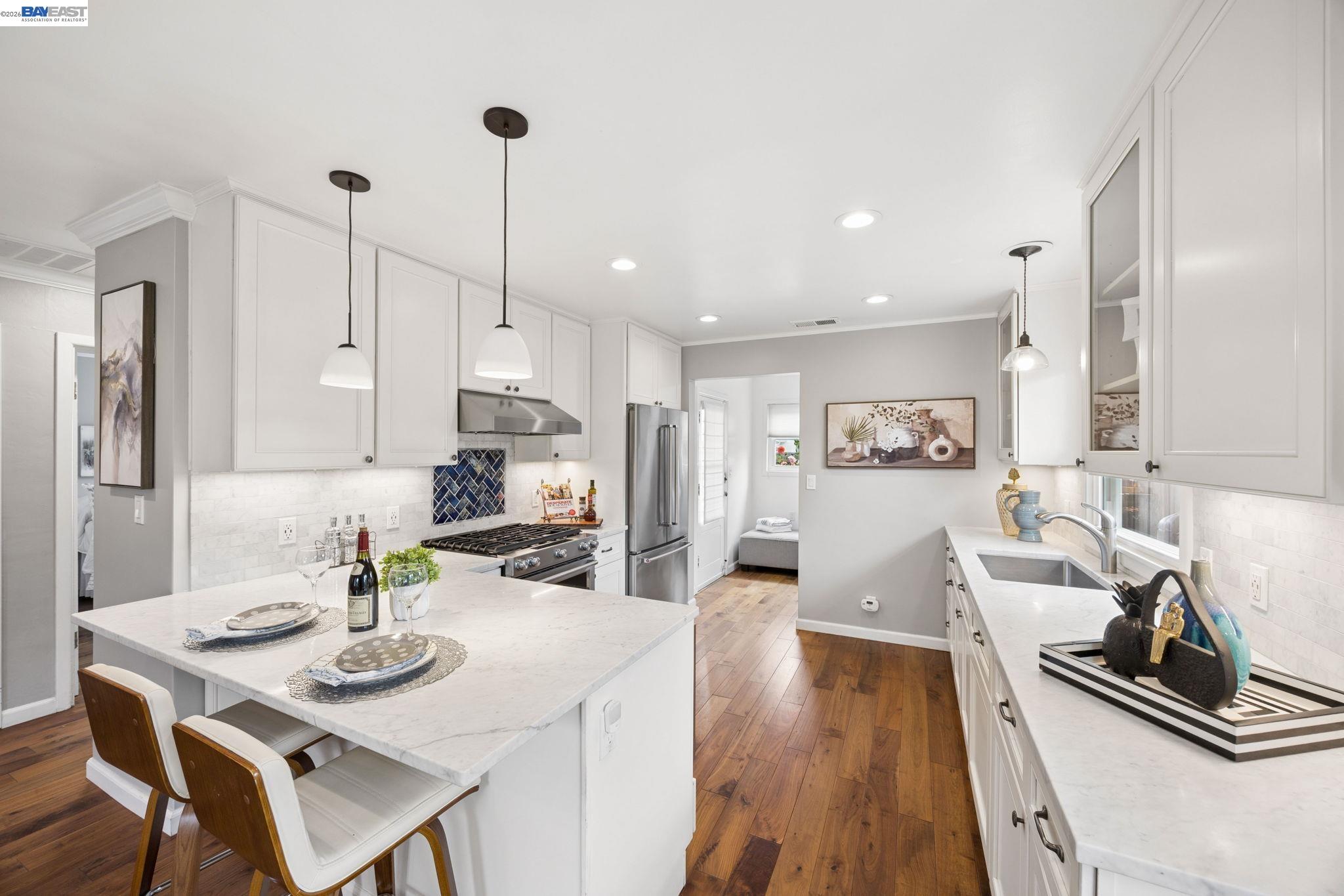 Bright white kitchen with a large island, stainless steel appliances, blue tile backsplash, and warm wood floors.