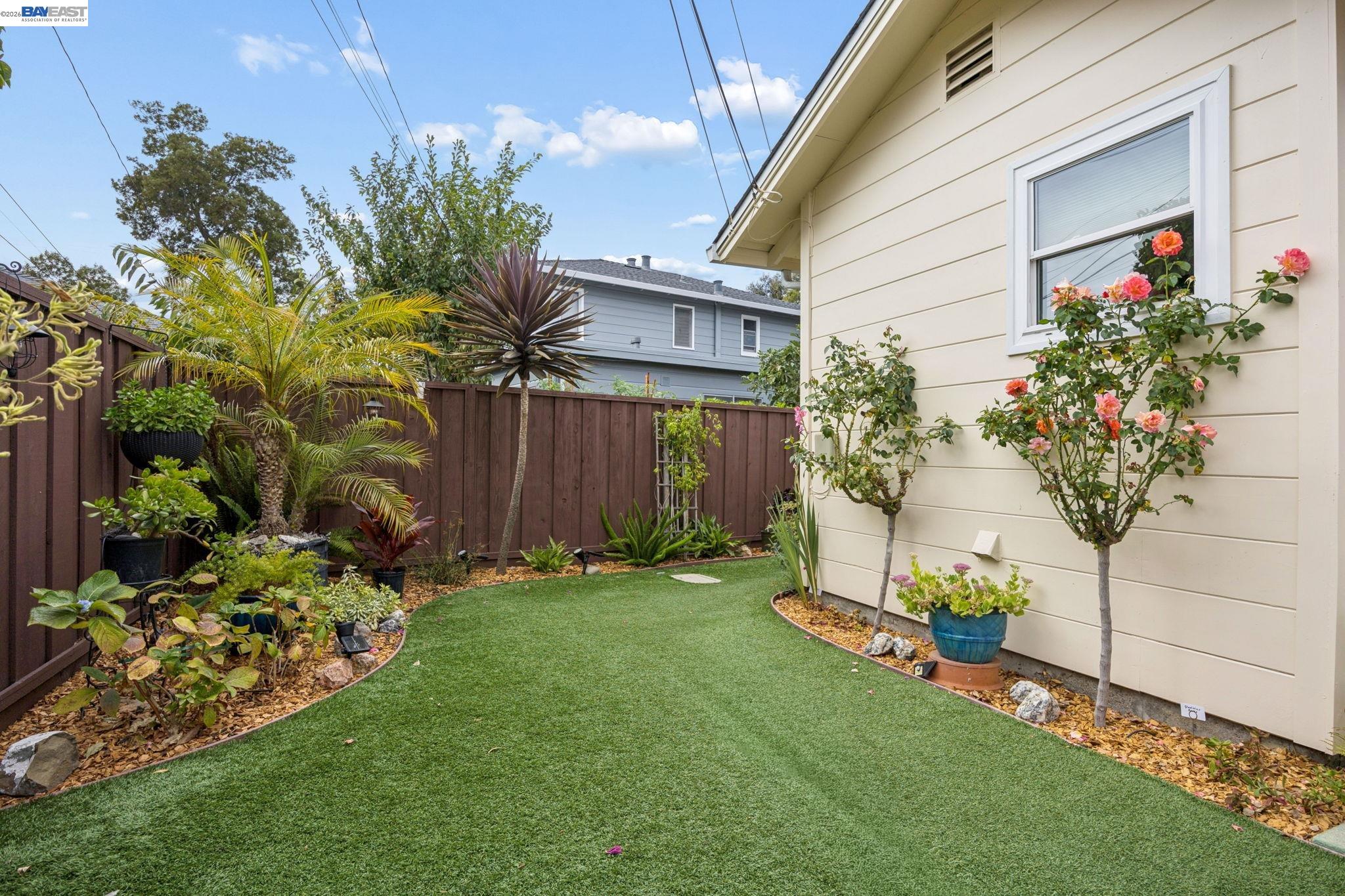 Side yard with a broad lawn, fenced garden, palms, and flowering roses beside the house.