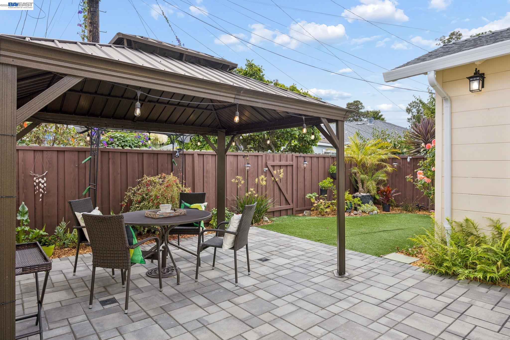Backyard patio with a covered pavilion, outdoor dining set, pavers, and fenced lawn.