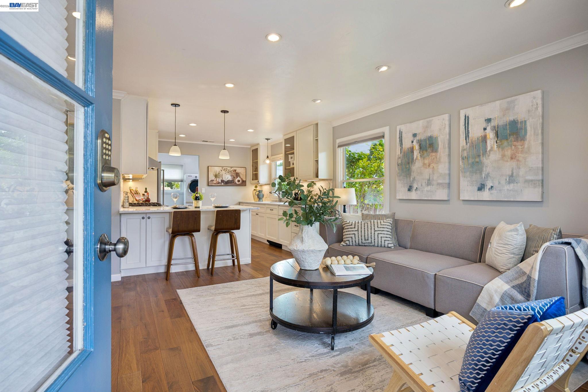 Open-plan living room and kitchen with a gray sectional, round coffee table, white cabinetry, and island seating.