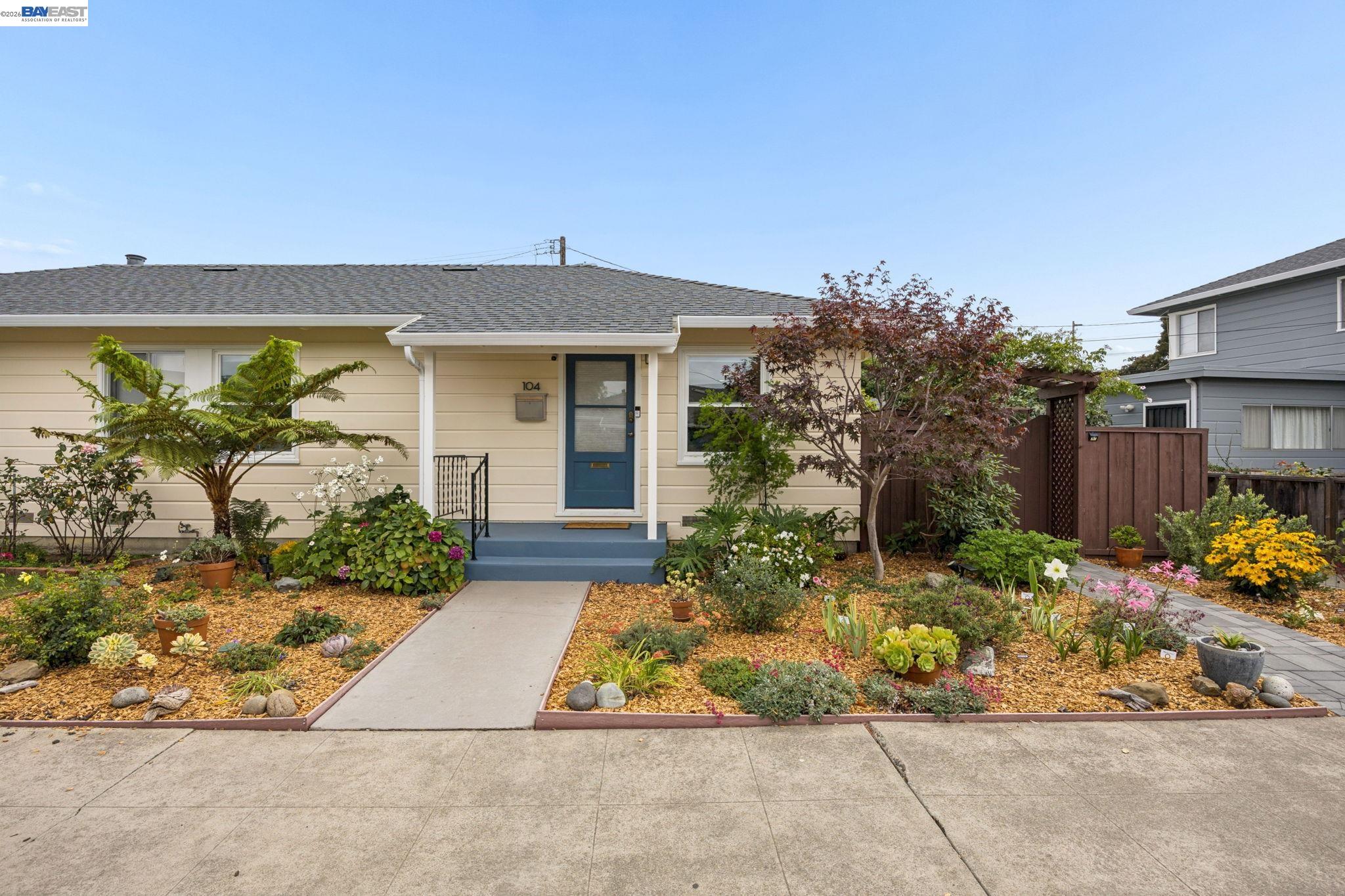 Single-story beige home with a blue front door and colorful landscaped garden.