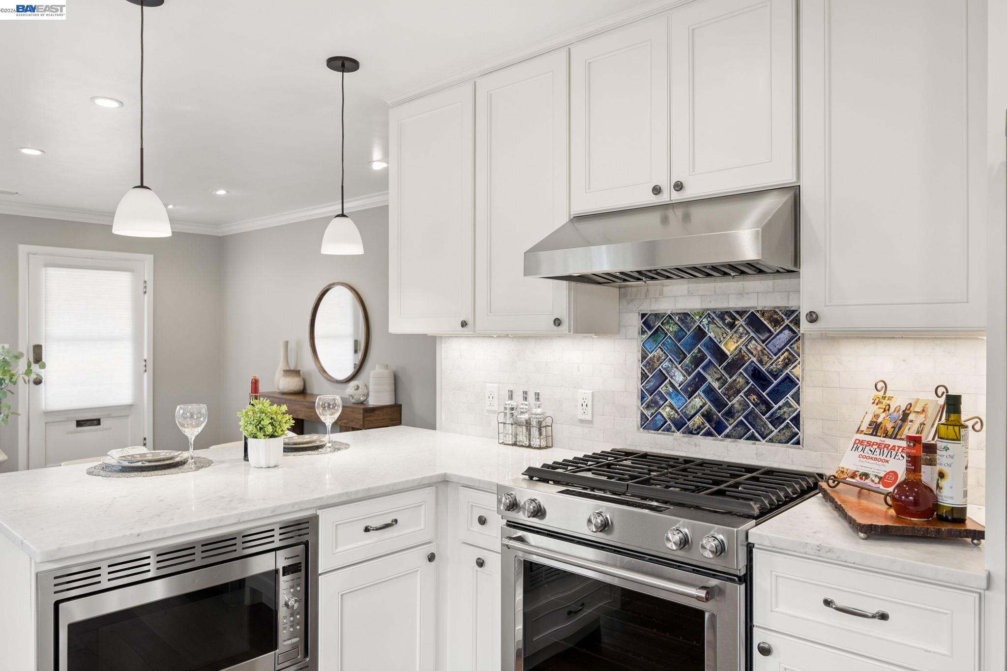 Bright white kitchen with a stainless-steel range, colorful tile backsplash, and a built-in island microwave.