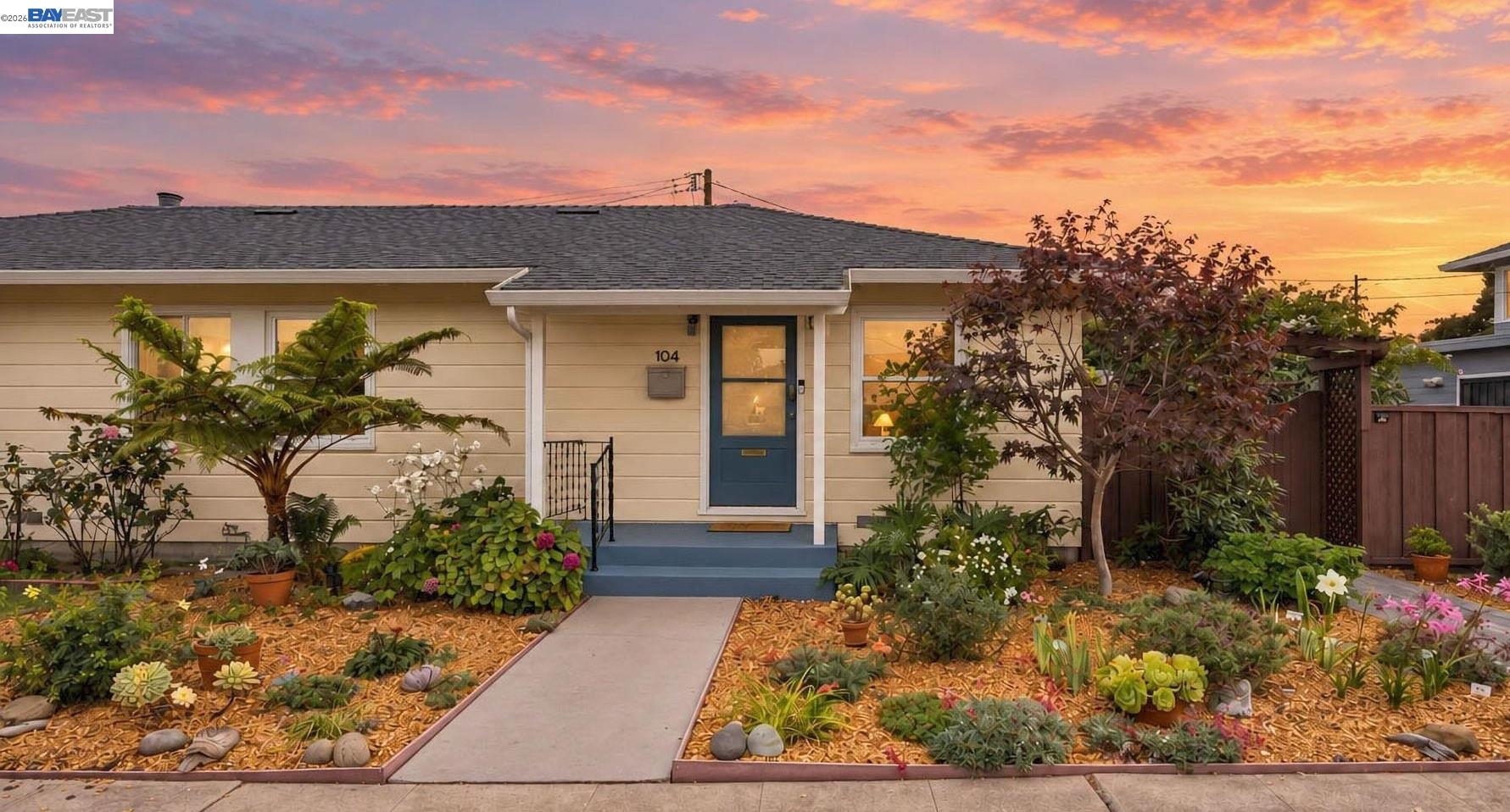 Single-story home with a blue front door and flower-filled garden at sunset.
