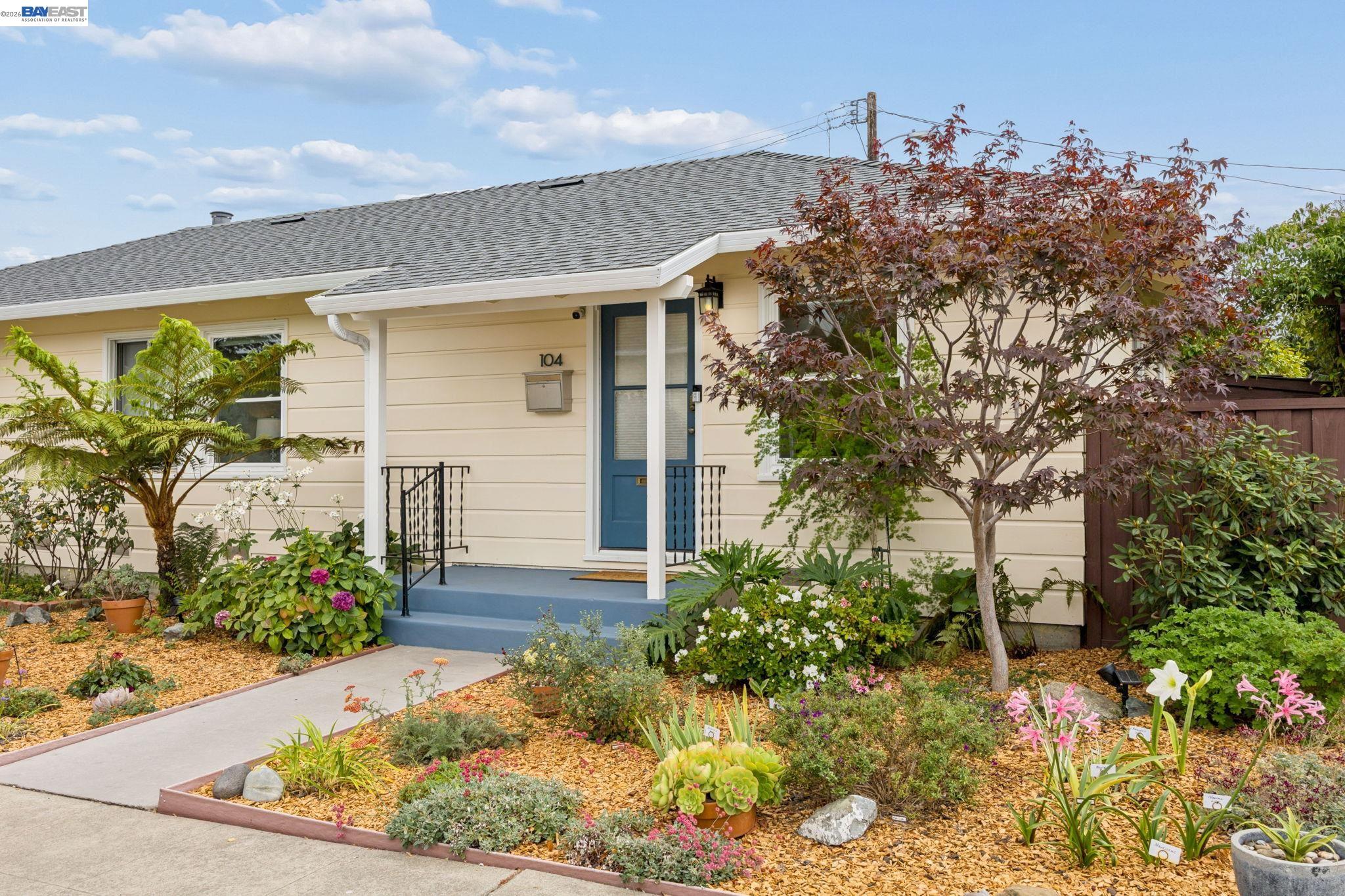 Cream-sided home with blue front door and a colorful landscaped garden.