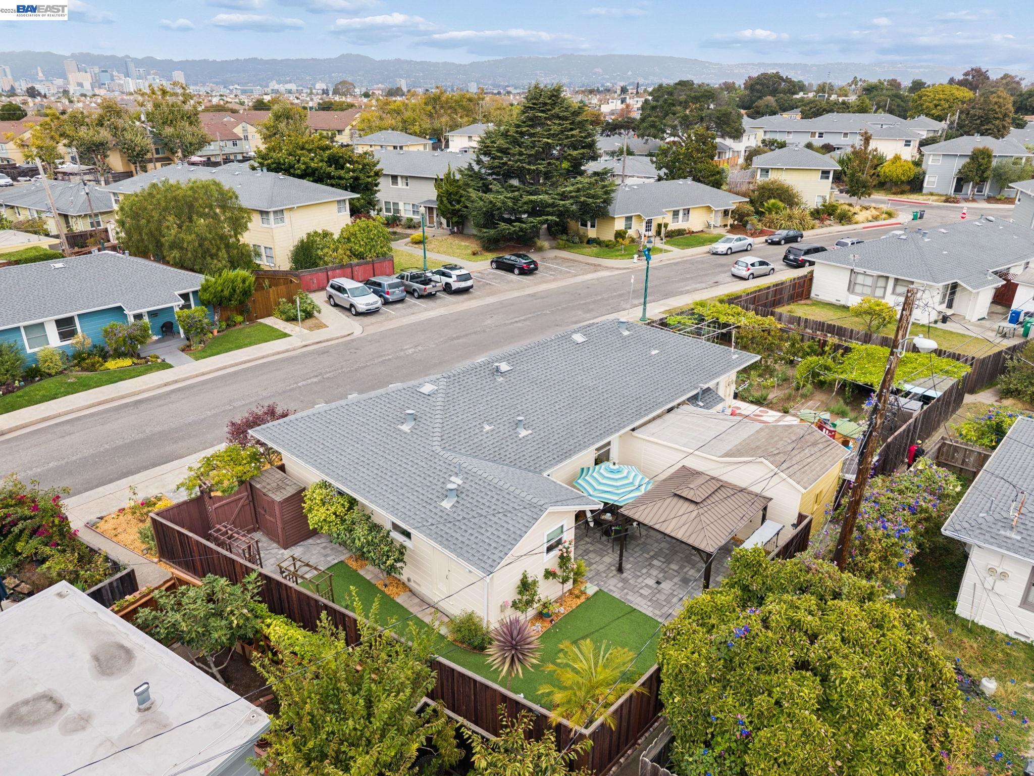 Aerial view of a landscaped backyard with a paved patio and pergola, overlooking a residential neighborhood and city skyline.
