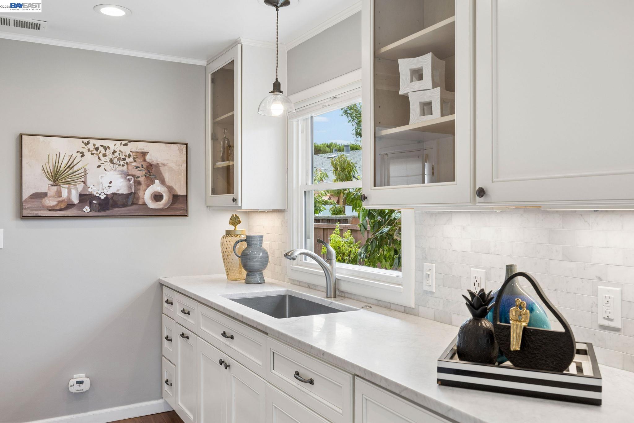 Kitchen with white cabinetry, marble counters, and a sink beneath a garden-facing window.