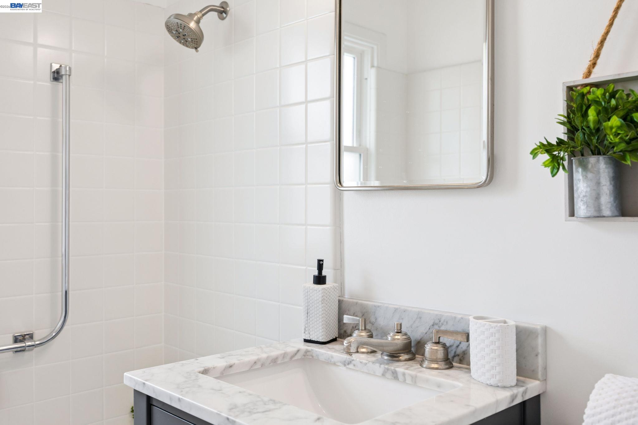 Bathroom vanity with marble countertop beside a white tiled shower and silver fixtures.