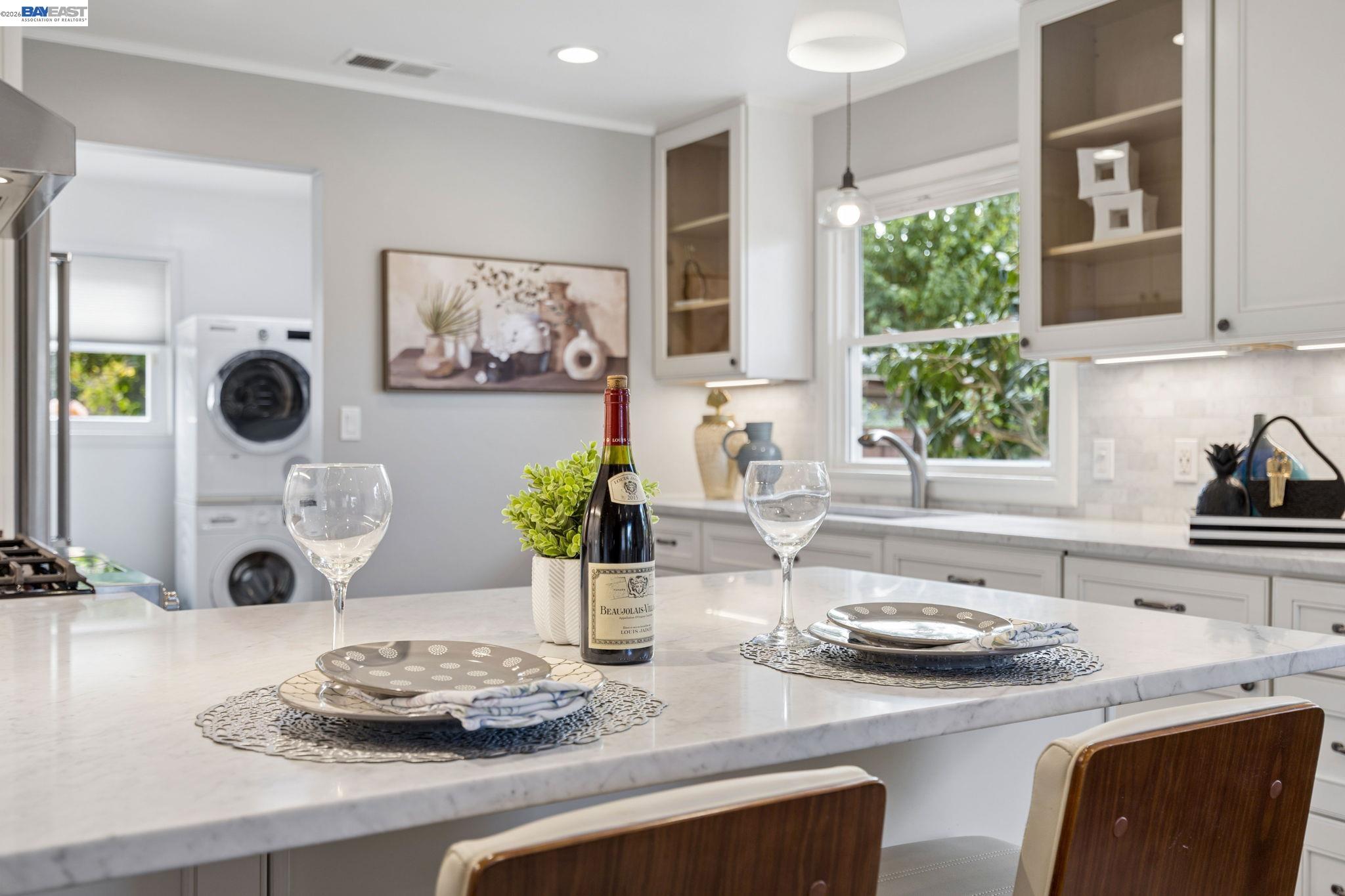 Bright white kitchen with a marble island set for two and a washer-dryer in the adjoining laundry area.