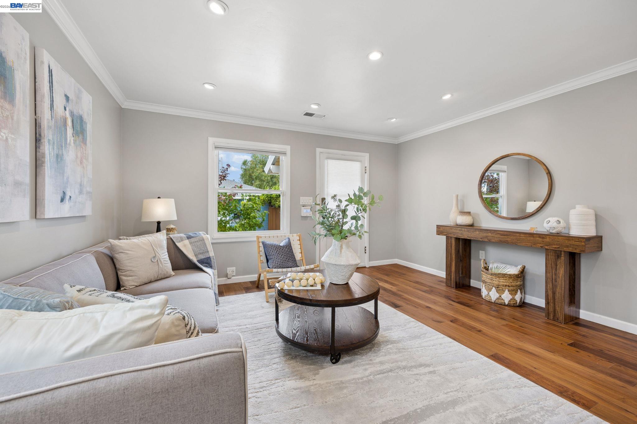 Staged living room with a gray sectional, round wooden coffee table, and console beneath a circular mirror.