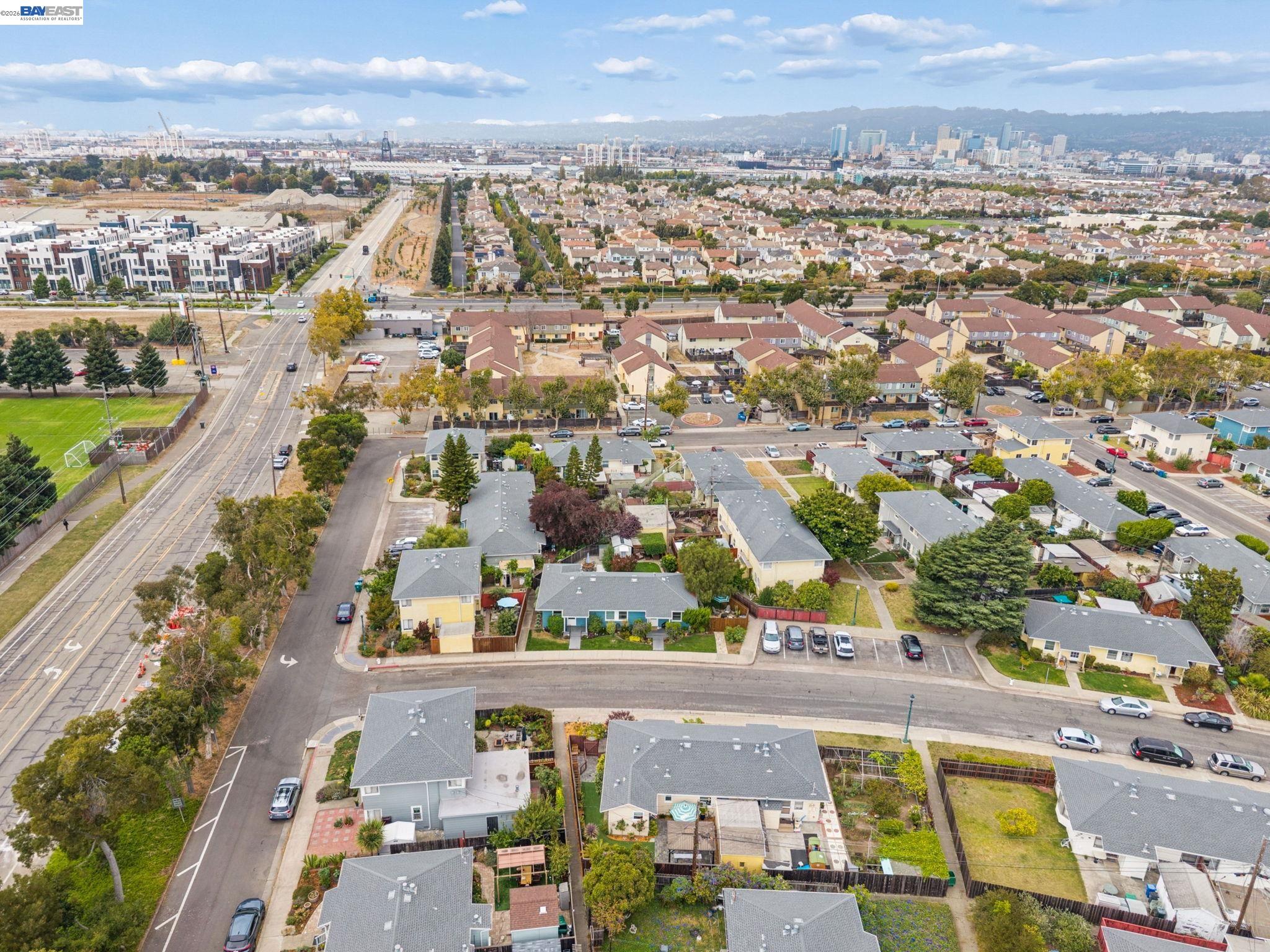 Aerial neighborhood view with rows of homes, a sports field, and distant city buildings.