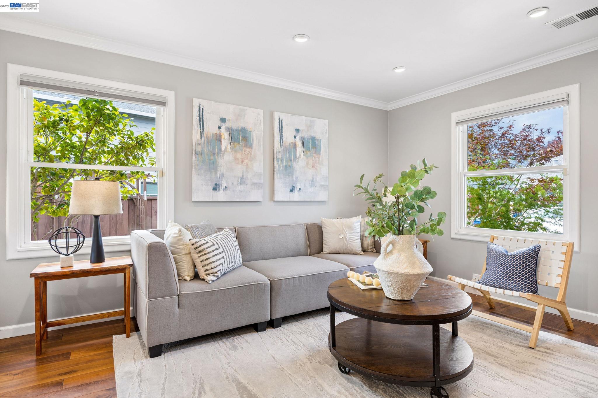 Staged living room with a gray sectional, round wooden coffee table, and windows overlooking trees.