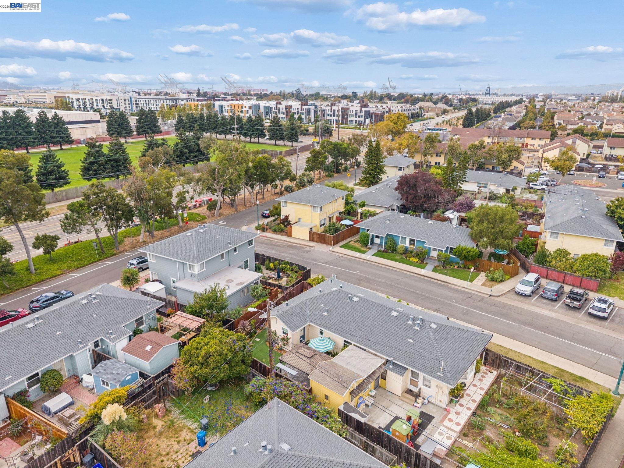 Aerial view of Alameda homes and tree-lined streets, with a park and port cranes in the distance.