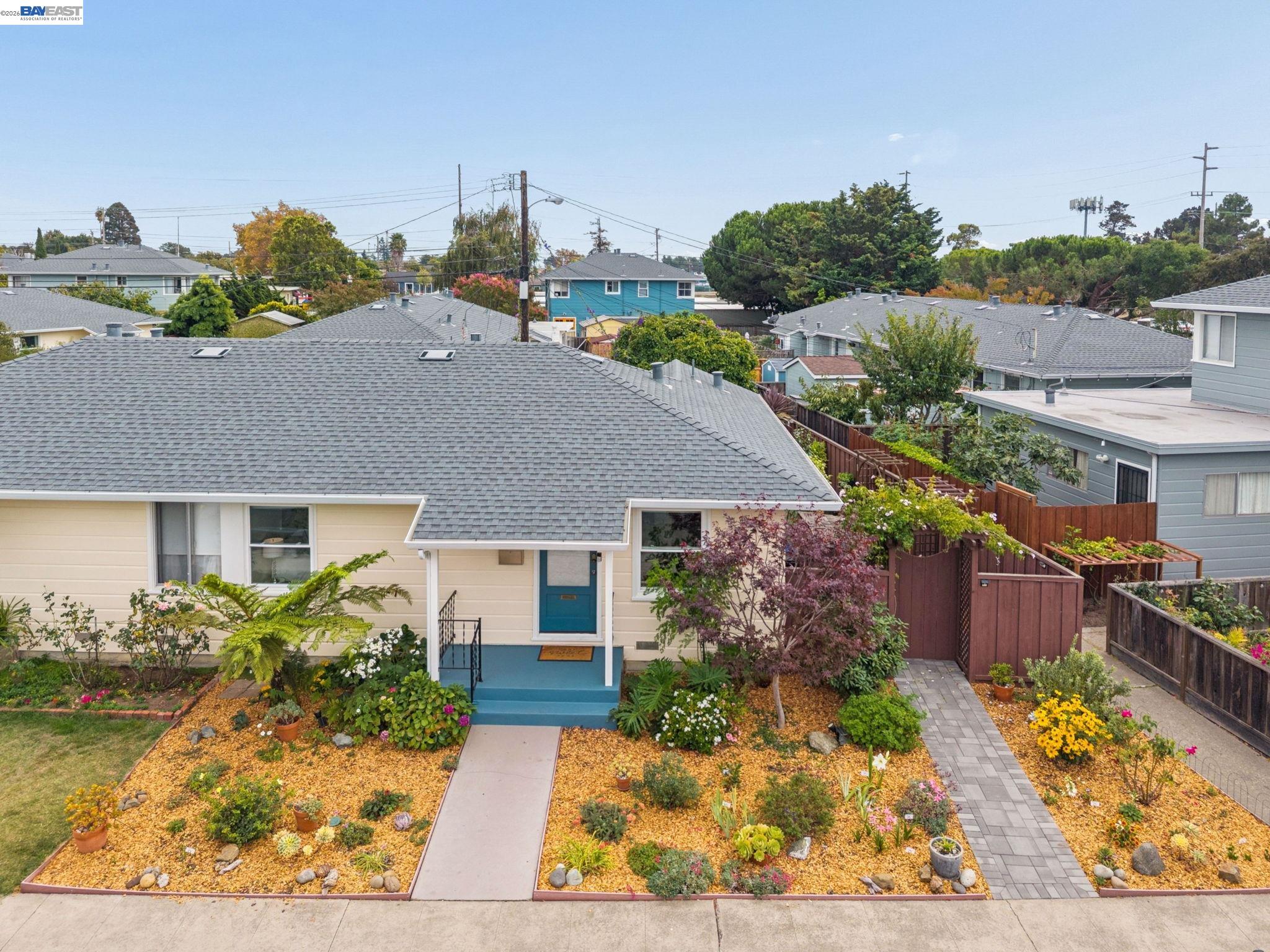 Single-story cream home with a teal front door, gray roof, and landscaped front garden.