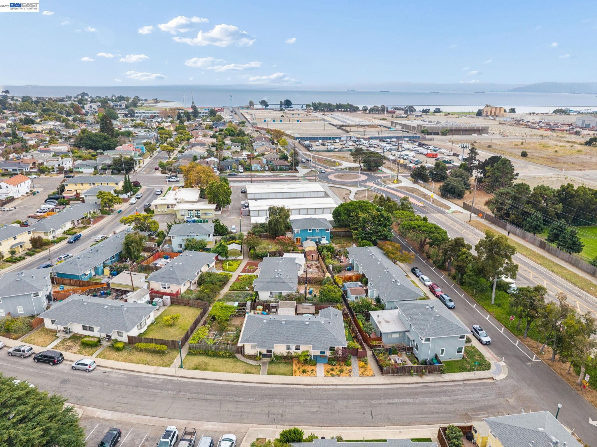 Aerial neighborhood view with the bay, nearby industrial buildings, and houses along a curved street.