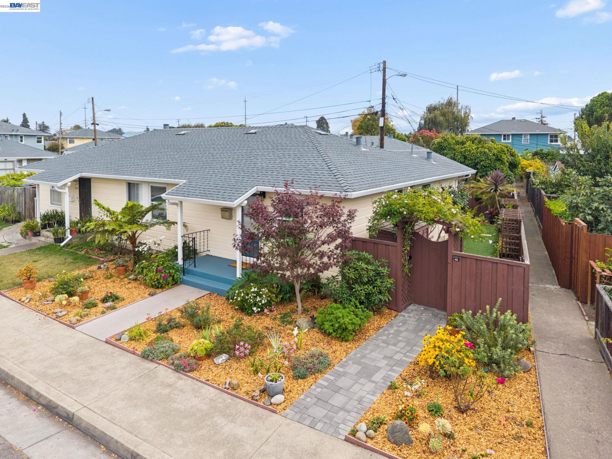 Single-story beige home with blue front steps and colorful landscaped gardens.