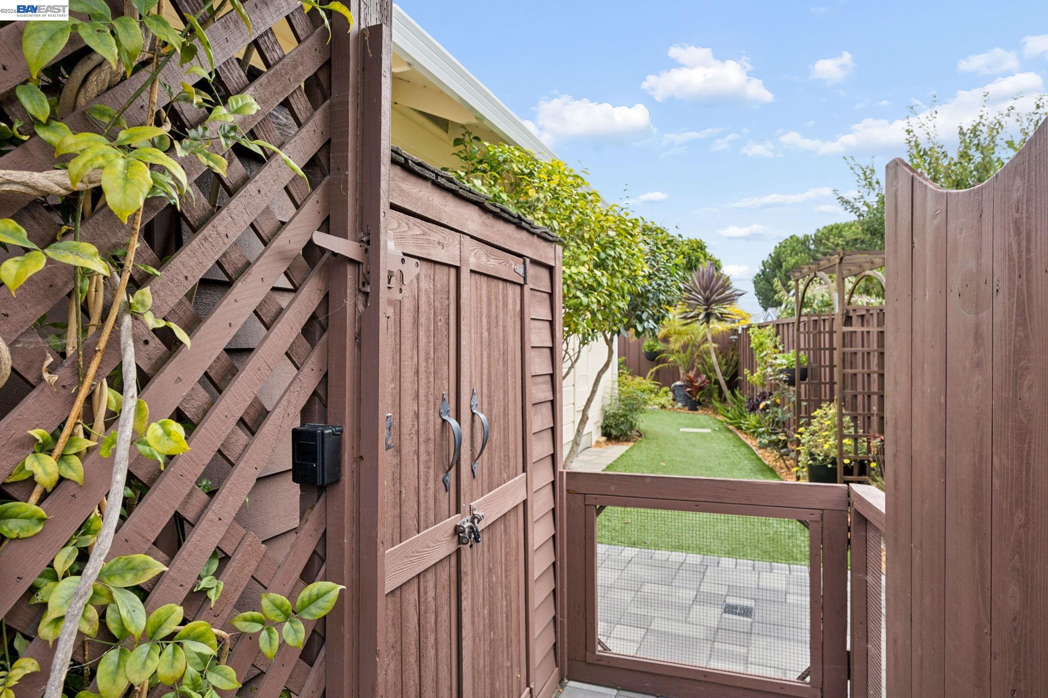 Landscaped side yard with a wooden gate, lattice fence, narrow lawn, and garden trellis.