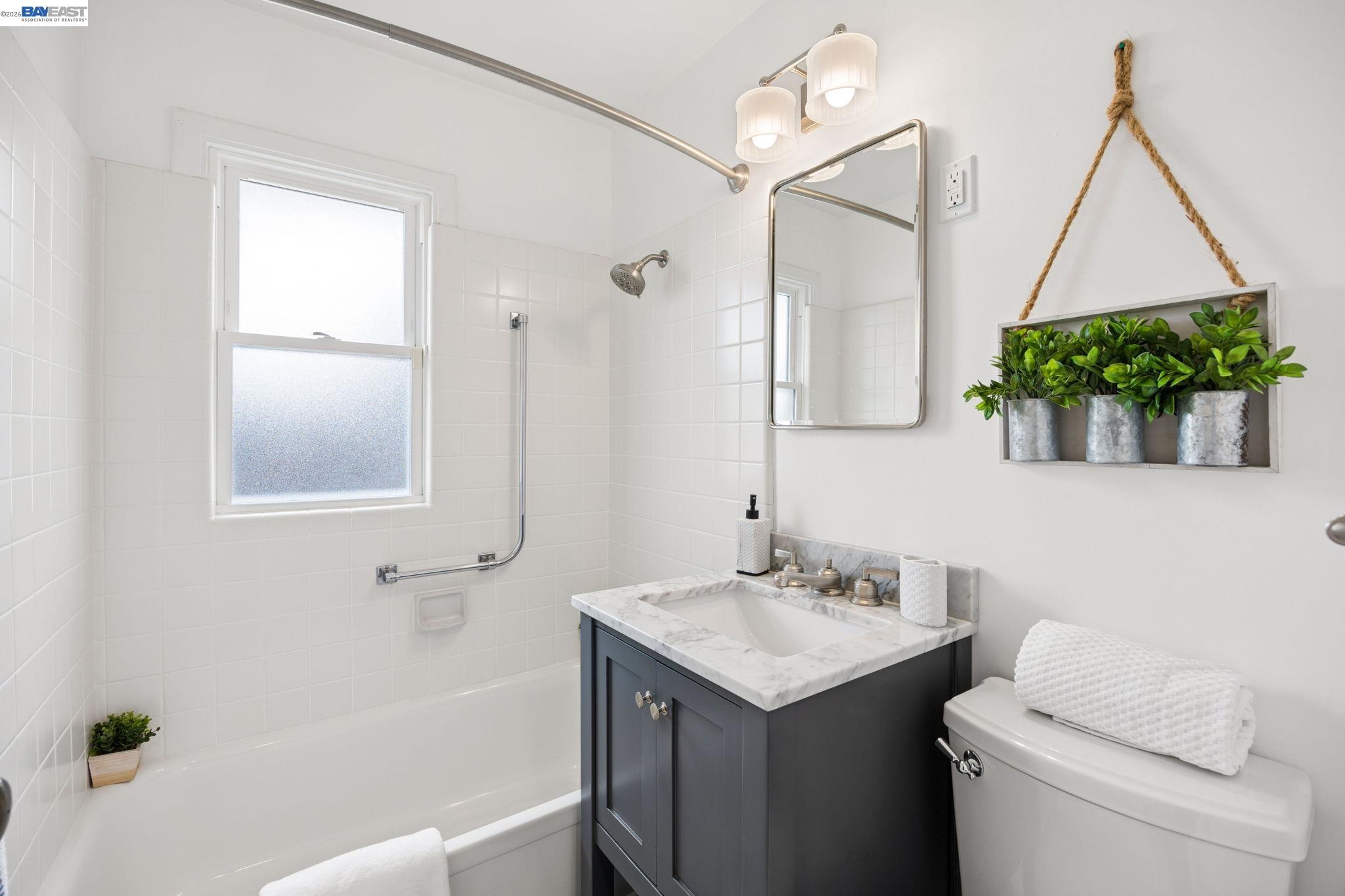 Bright bathroom with tiled tub, frosted window, and dark vanity topped with marble.
