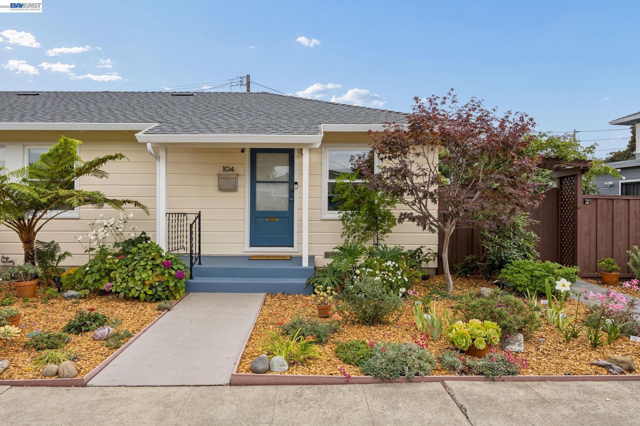 Beige single-story home with a blue front door, covered entry, and colorful landscaped garden.