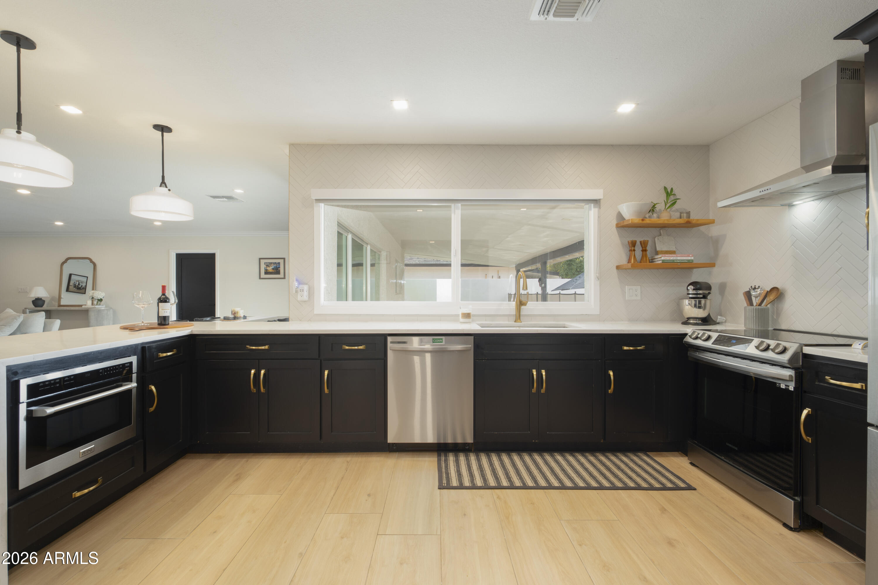 Modern kitchen with black cabinets, brass hardware, stainless steel appliances, and a wide window to the patio.