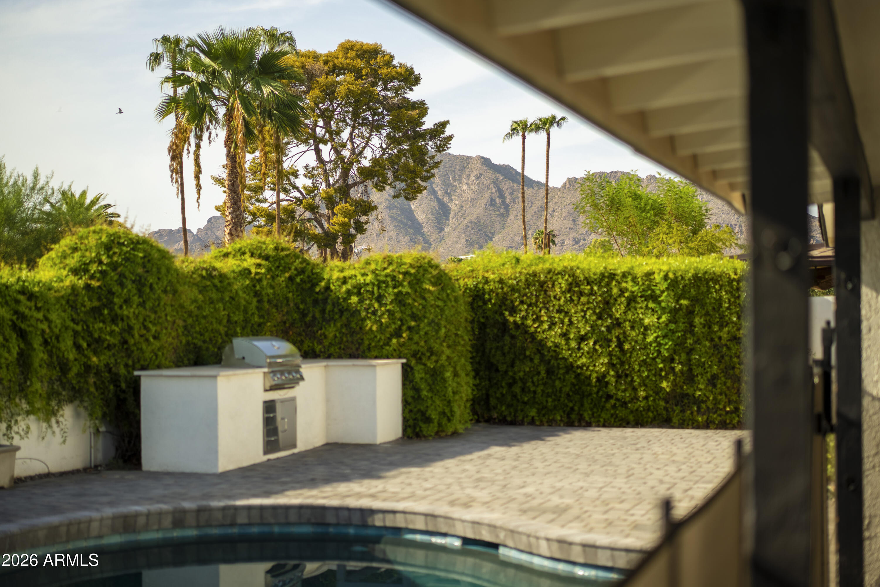 Backyard pool and patio with a built-in grill, privacy hedges, and mountain views.