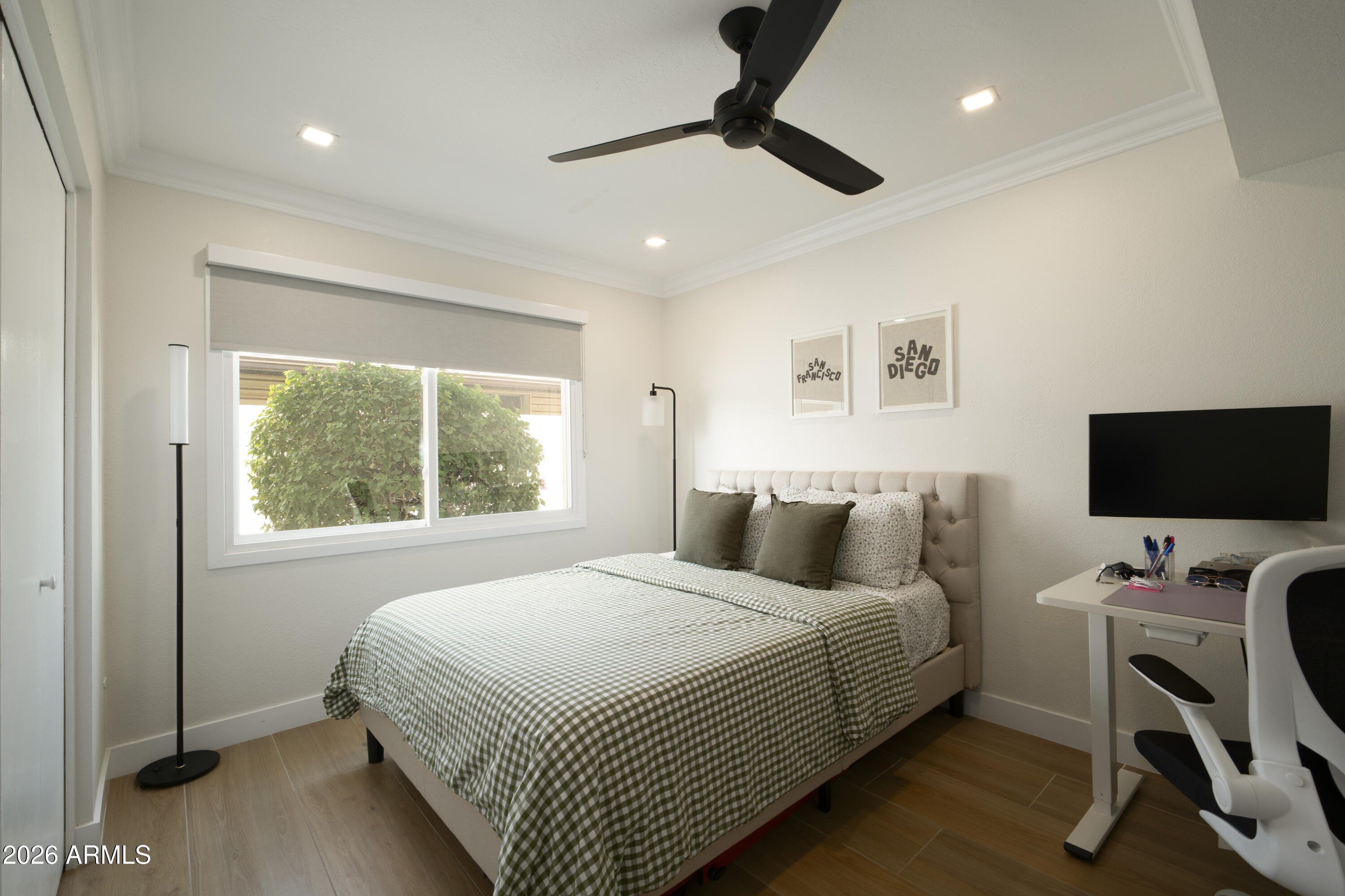 Furnished bedroom with a checked duvet, large window, and desk with monitor.