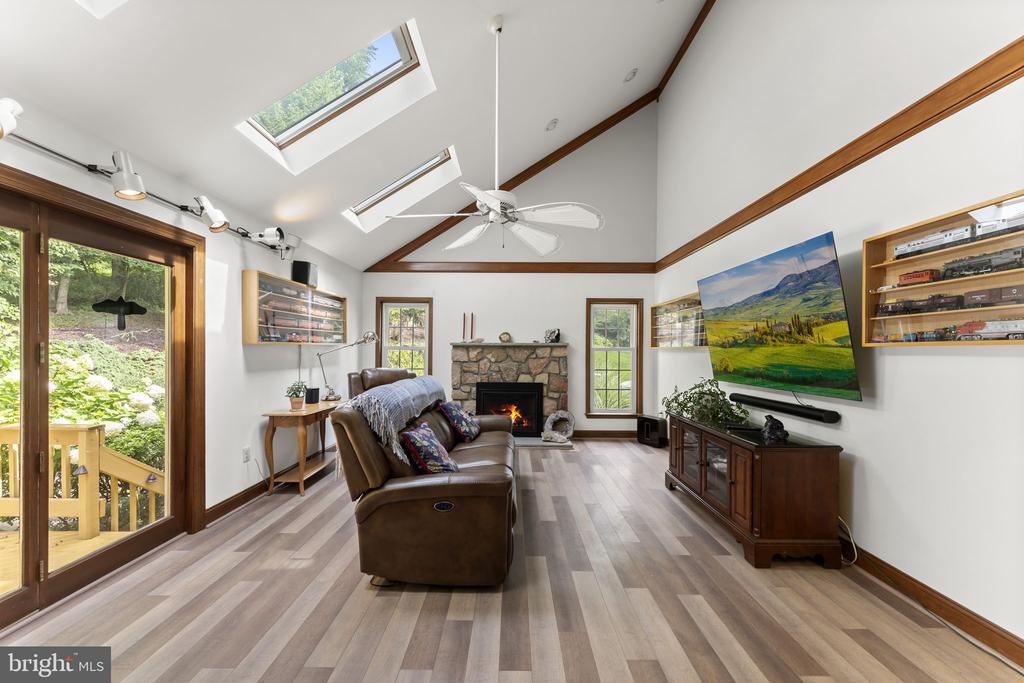 Living room with vaulted skylit ceiling, stone fireplace, and sliding glass doors to a wooded deck.