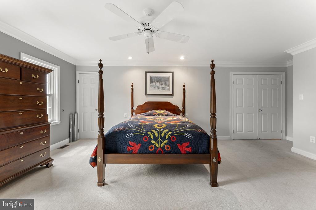 Bedroom with a dark wood four-poster bed and colorful floral quilt, gray walls, and light carpet.