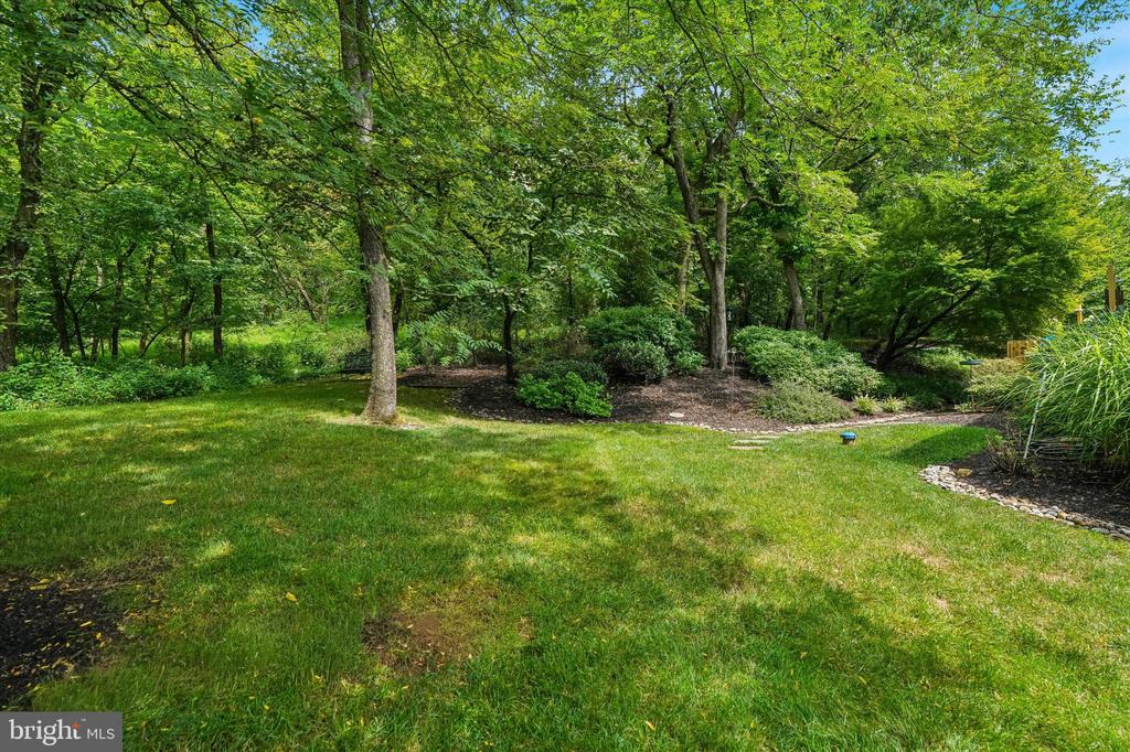 Landscaped backyard with a broad lawn, mature trees, shrubs, and a rock-edged garden bed.