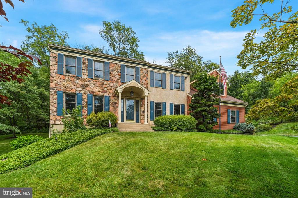 Two-story stone-front home with blue shutters, covered entry, and a broad lawn.