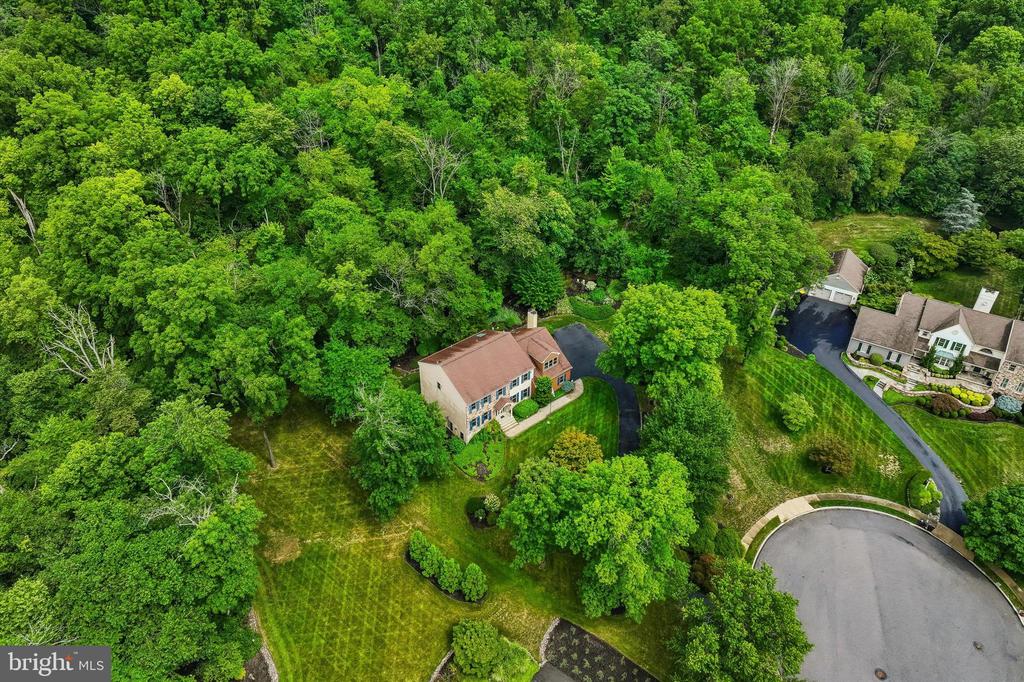 Aerial view of a two-story home amid dense trees, with its driveway and cul-de-sac visible.