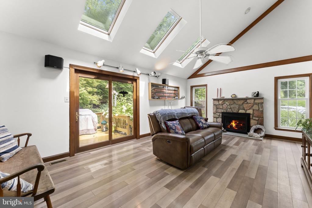 Living room with a stone fireplace, skylights, vaulted wood-beam ceiling, and sliding glass doors to a deck.