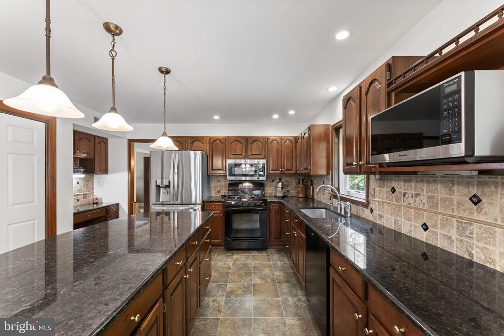 Kitchen with dark wood cabinets, granite counters, a large island, and stainless steel appliances.