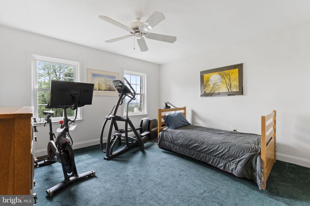 Bedroom with a single bed and exercise equipment beside two windows.