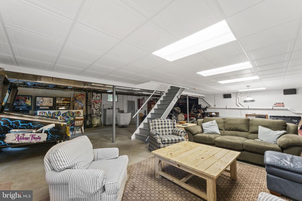 Basement recreation room with pinball machines, a sectional sofa, striped armchairs, and a wooden coffee table.