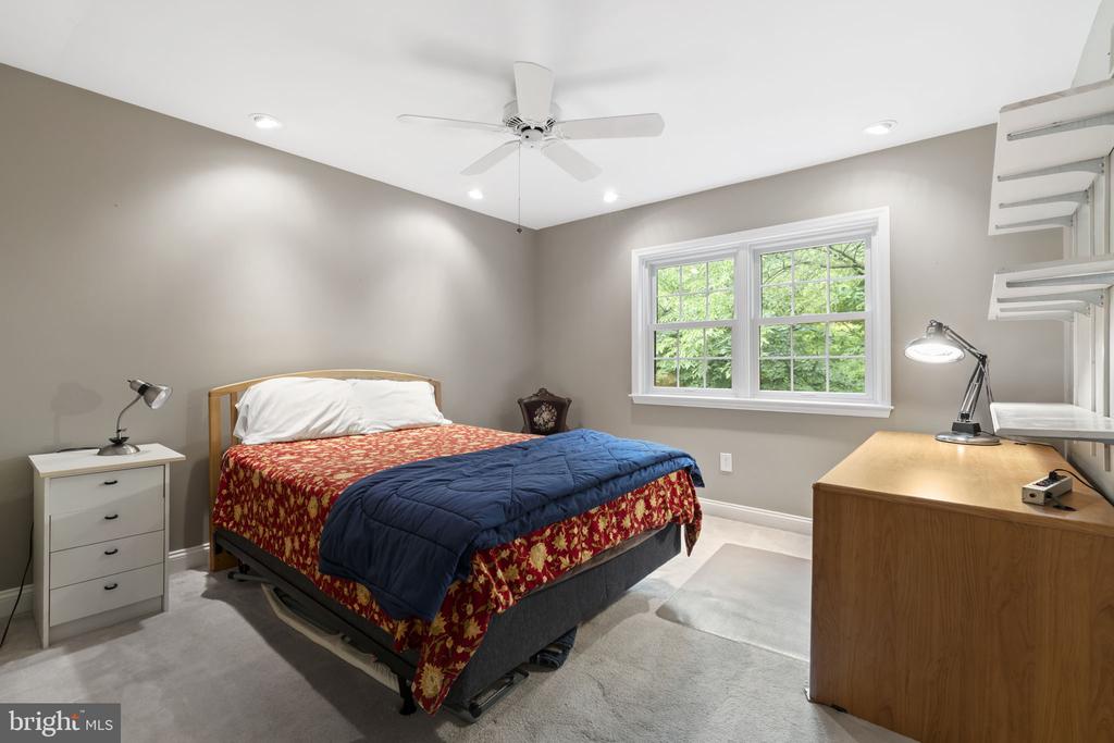 Bedroom with a red floral bedspread, navy comforter, and large window overlooking greenery.