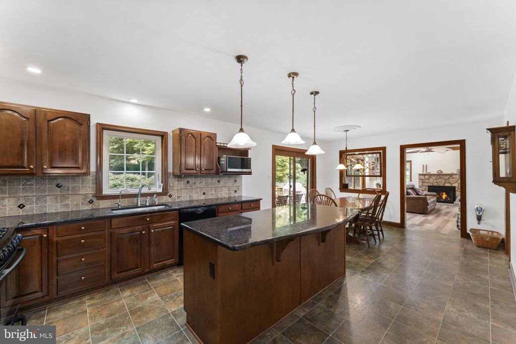 Kitchen with dark wood cabinets and a large granite island opening to a dining area.
