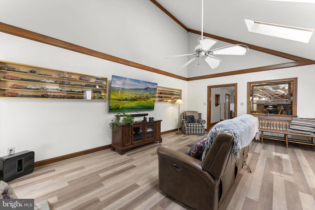 Living room with vaulted wood-beamed ceiling, light plank floors, wall-mounted television, and reclining seating.