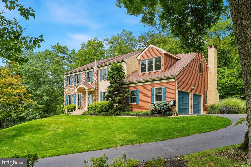 Two-story stone and orange-sided home with blue shutters, a green lawn, and a curved driveway.