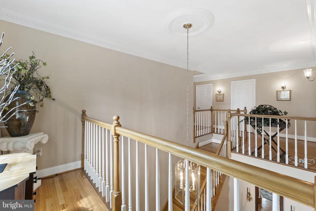 Upstairs landing overlooking a staircase, with hardwood floors and white balusters topped by a wood handrail.