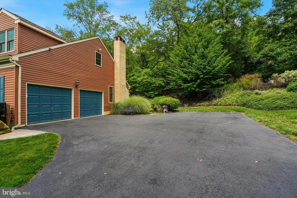 Red-sided house with two blue garage doors beside a broad driveway and mature trees.