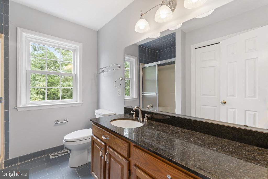 Bathroom with a wood vanity, dark stone countertop, large window, and tree views.