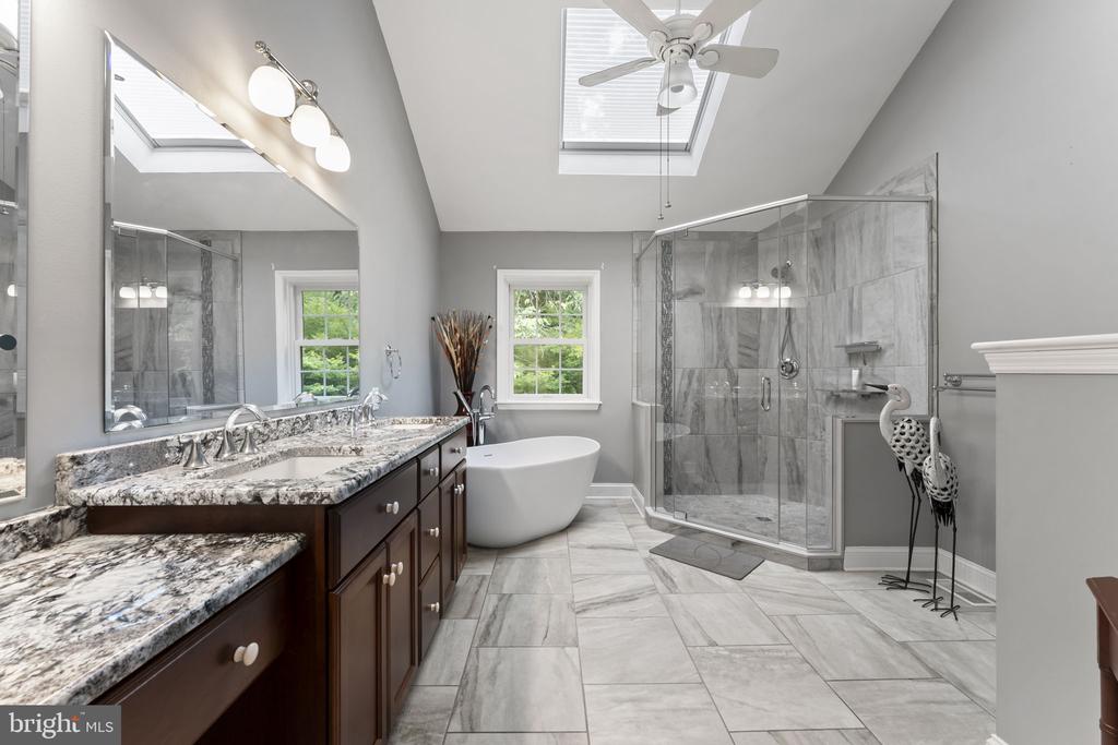 Bathroom with a double vanity, freestanding tub, glass shower, and two skylights.