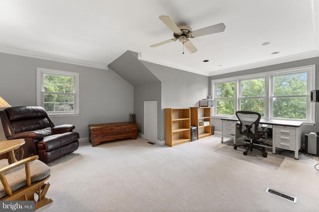 Spacious carpeted office with a desk beneath three large windows, wooden bookcases, and a leather recliner.
