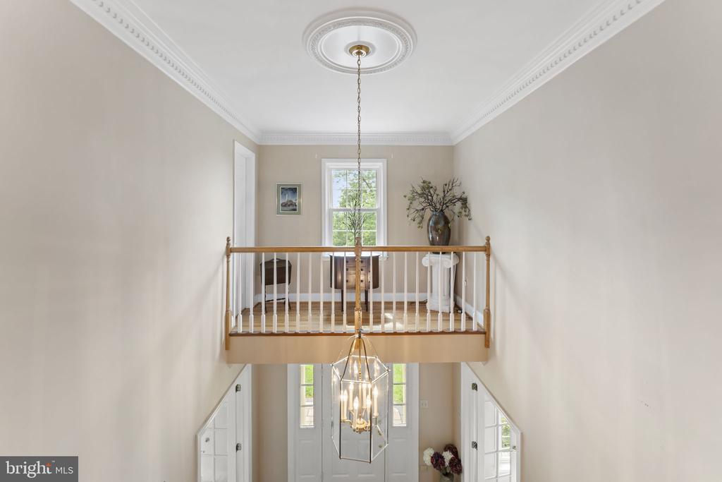 Upper landing overlooking a two-story foyer, with a wood-and-white railing and hanging chandelier.